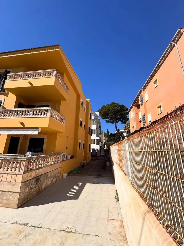 Edificio de apartamentos pintado de amarillo con balcones de balaustres, visto desde un callejón