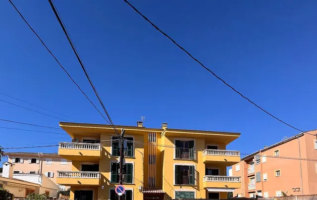 Edificio amarillo de tres plantas con balcones de balaustres, visto desde la calle