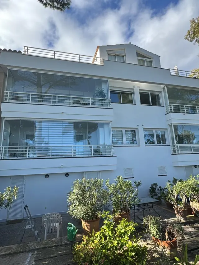 Edificio blanco de varias plantas con terrazas acristaladas y plantas