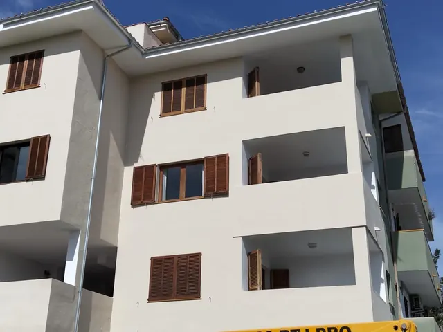 Edificio blanco de cuatro plantas con balcones y contraventanas de madera