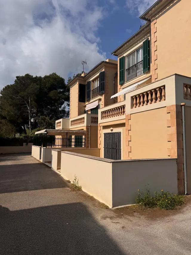 Villa de dos plantas en ocre y crema, con balaustres en las terrazas, vista desde la calle