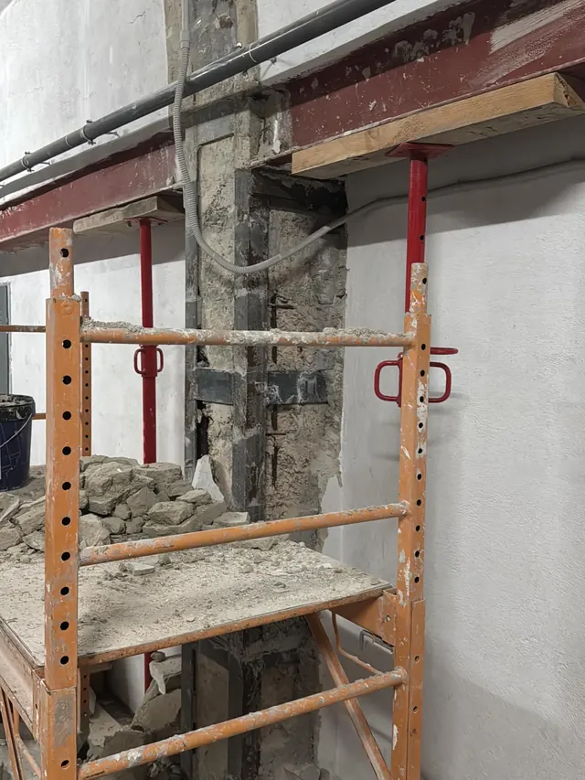Andamio bajo junto a un pilar en obra, con viga roja y puntal