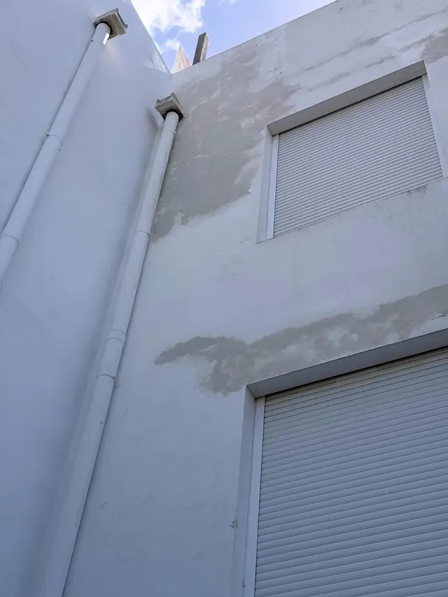 Bajante con reparaciones de revoque junto a una ventana con persiana