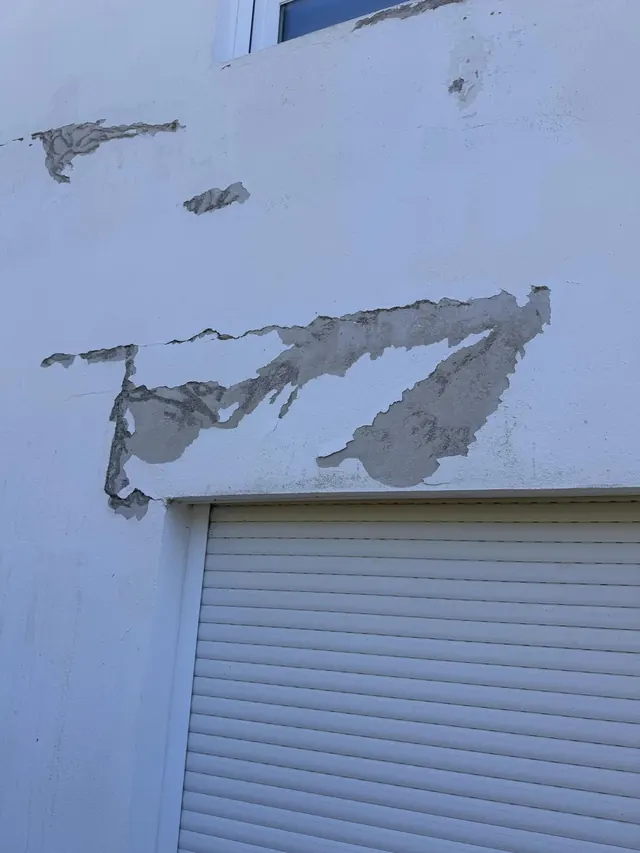 Pintura y revoque desconchados bajo una ventana con persiana