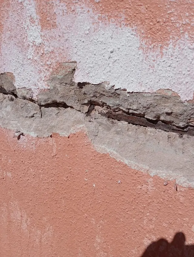 Detalle de una grieta y de revoque desprendido en una fachada de color salmón