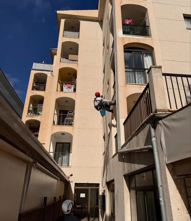 Operario en cuerda trabajando junto a un balcón en la fachada de un edificio de cinco plantas
