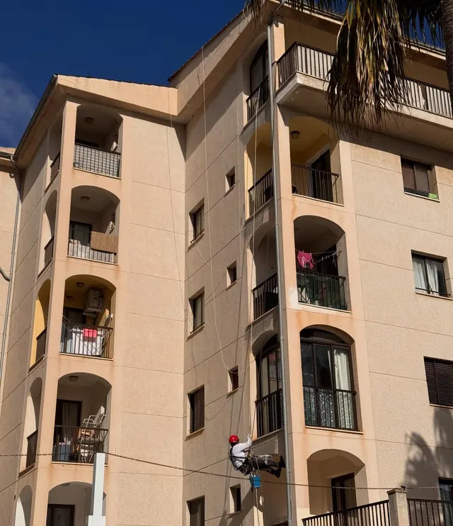 Edificio salmón de cinco plantas con un operario trabajando en cuerda a media altura